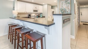 Eine Küche mit weißen Schränken, einer Granit-Arbeitsplatte und einer Bar mit Barhocker.