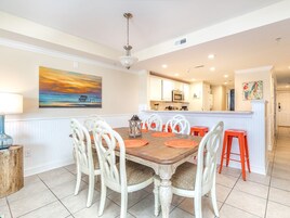 A dining area with a wooden table, white chairs, and orange placemats.