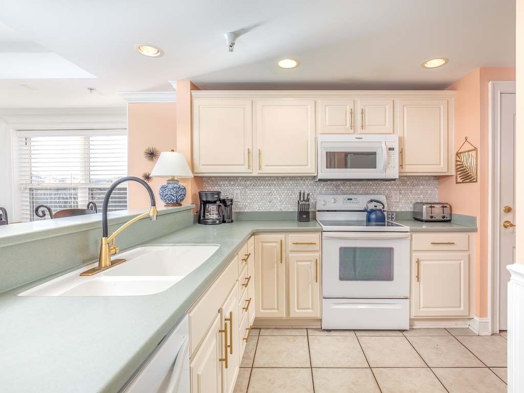 A kitchen with white cabinets, a microwave, a stove, and a sink with a gold faucet.