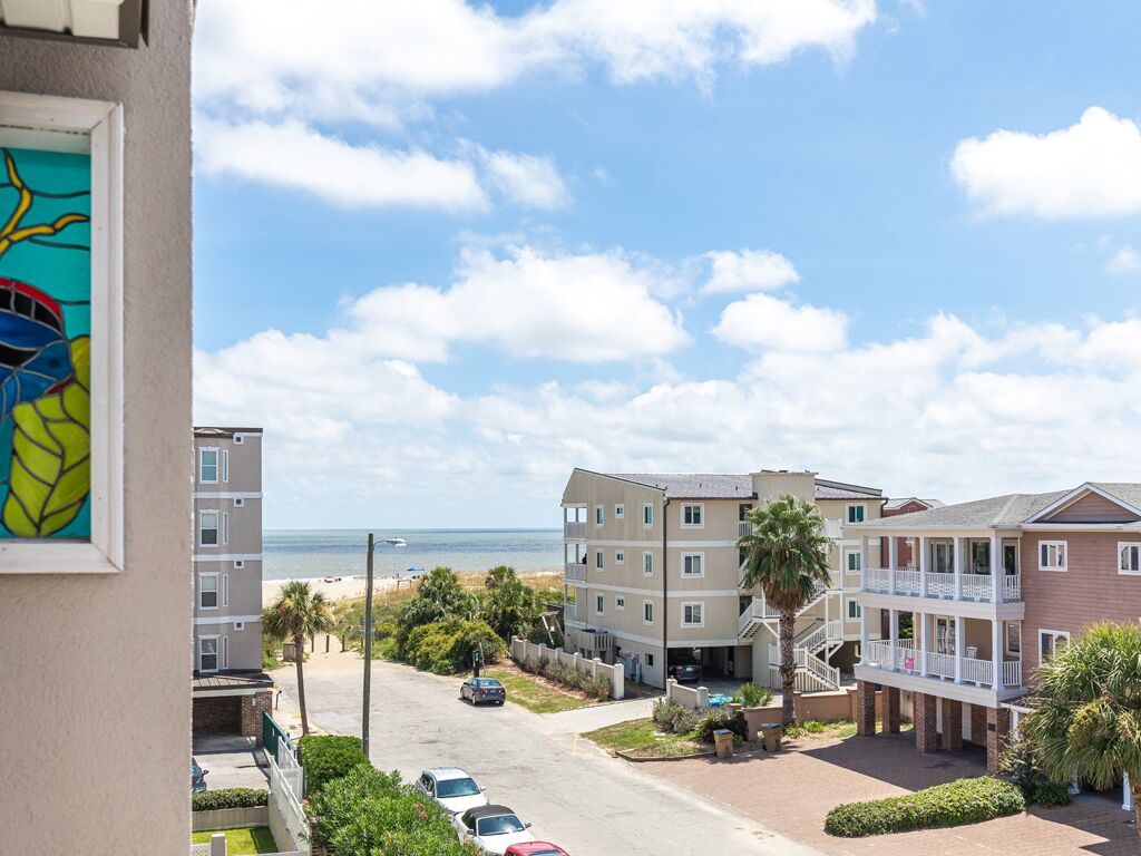 A multi-story building with a balcony, a parking area, and a view of the beach.