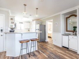 A kitchen with white cabinetry, a central island with stools, and a refrigerator.