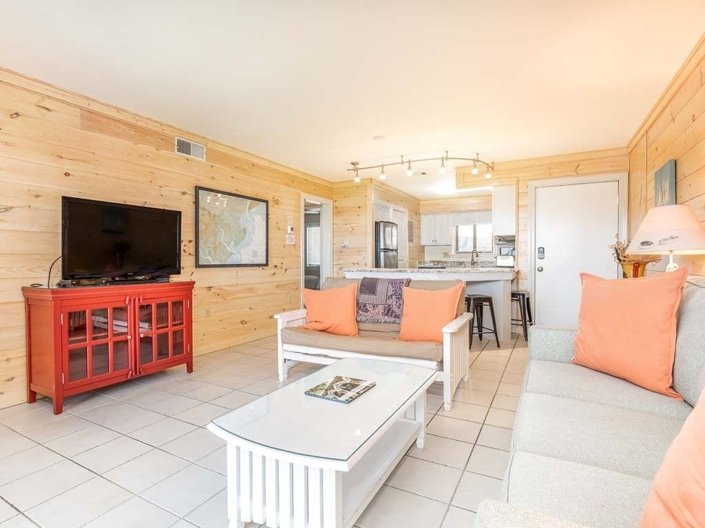 A cozy living room with a television, a red cabinet, and a white sofa with orange cushions.