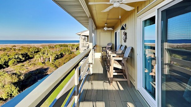 A balcony with a view of the beach, a ceiling fan, and a table with chairs. - Lighthouse Point 1 by Tybee Vacation Rentals (Tybee Island)