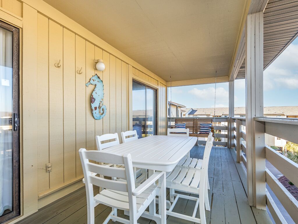 A covered outdoor area with a white table and chairs, a seahorse decoration, and a view of the beach.