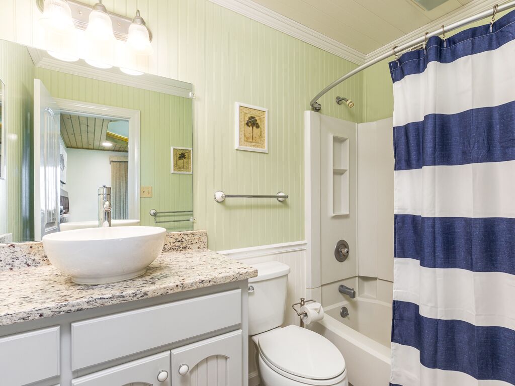 A bathroom with a white sink, a toilet, a shower, and a striped shower curtain.