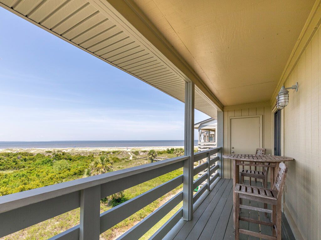 A covered balcony with a view of the beach, a wooden table, and chairs.