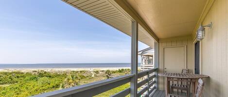 A covered balcony with a view of the beach, a wooden table, and chairs.