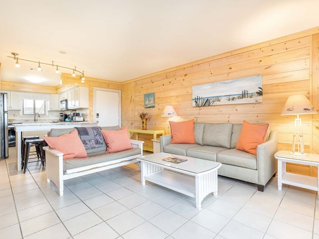 A modern living room with a sofa, a coffee table, and a dining area with a kitchen in the background.