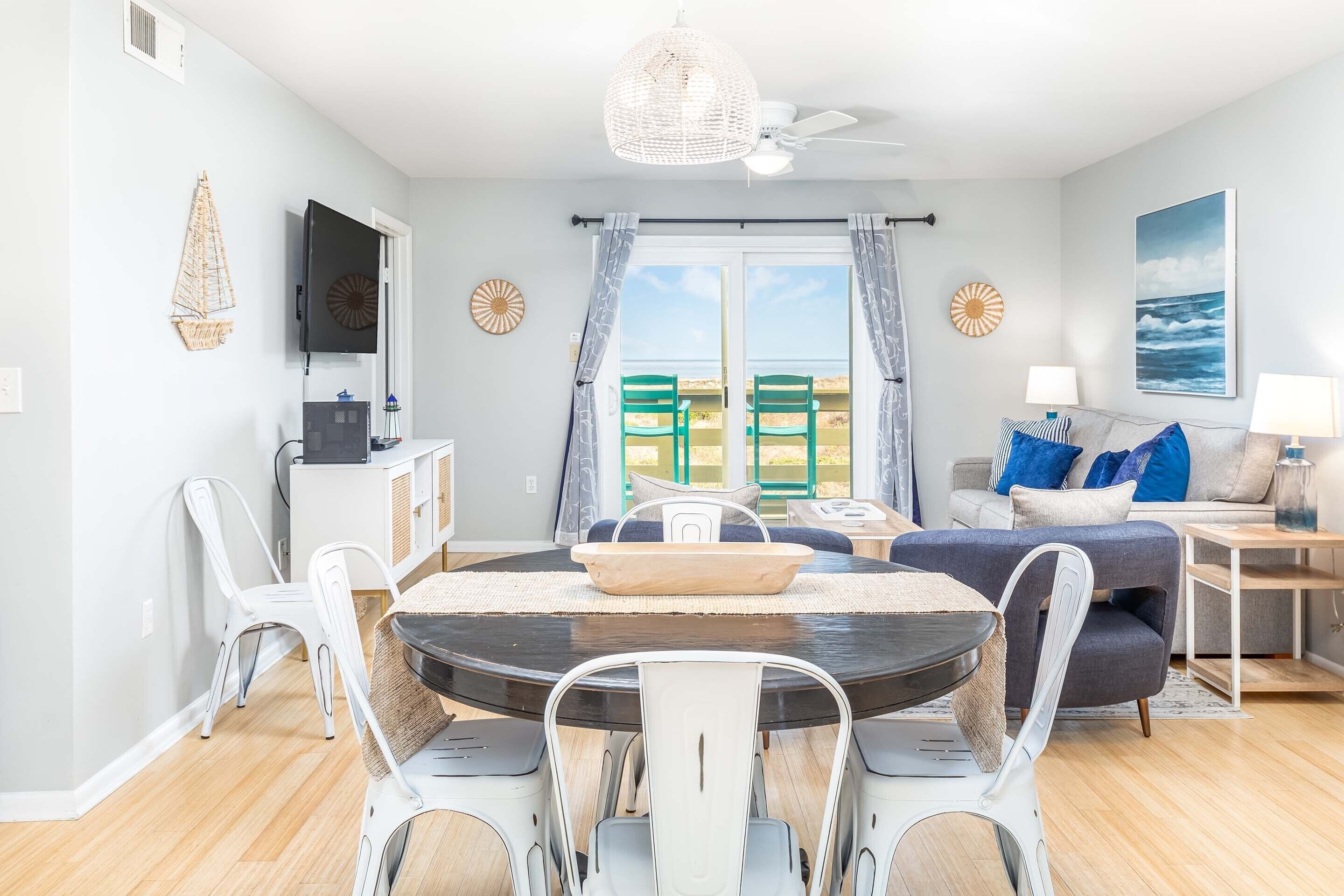 A modern living room with a dining area, a television, and a view of the sea through large windows.