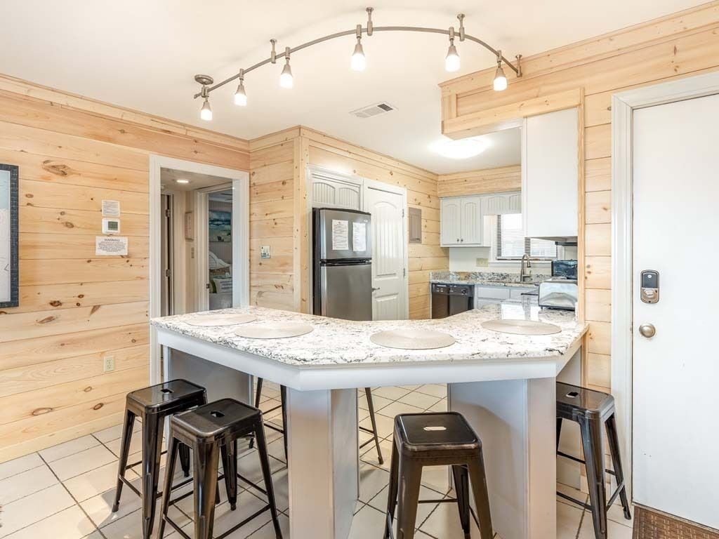 Una cocina moderna con una isla central, taburetes de bar, paneles de madera y electrodomésticos integrados.