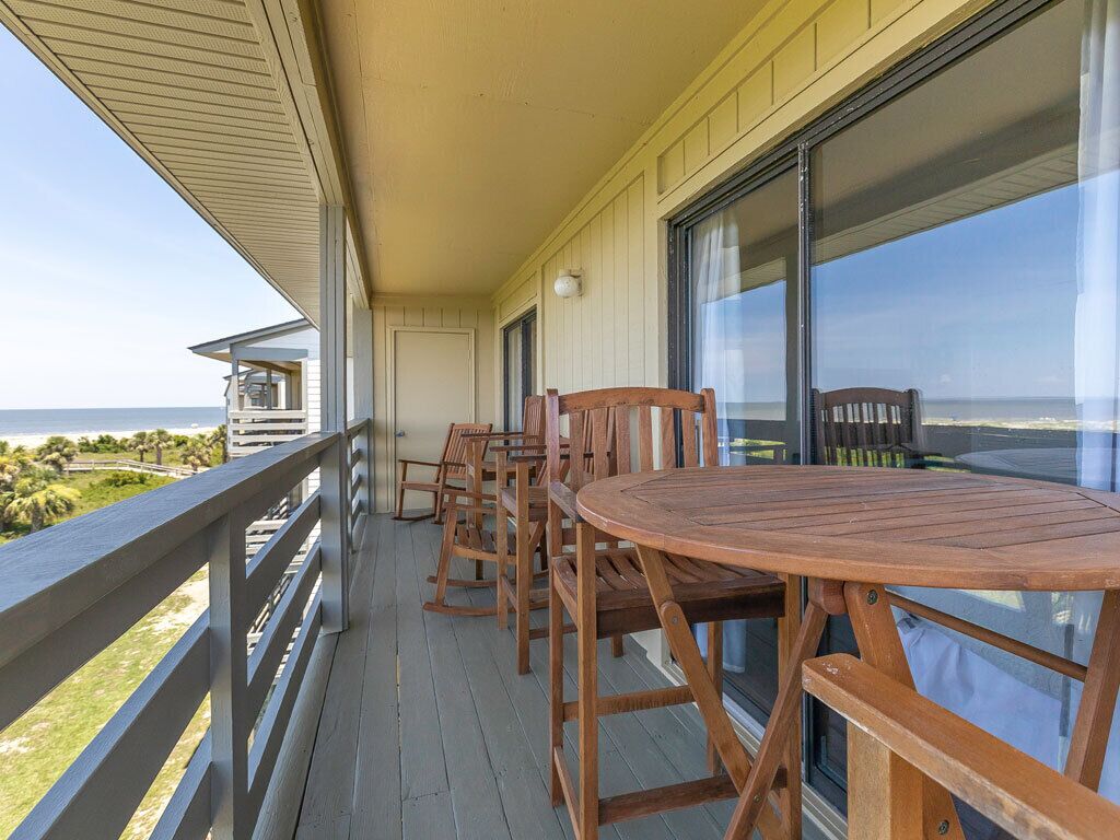 A wooden deck with a round table and chairs, overlooking a beach and ocean.