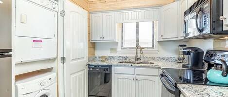 Una cocina compacta con muebles blancos, horno empotrado, microondas y lavavajillas.
