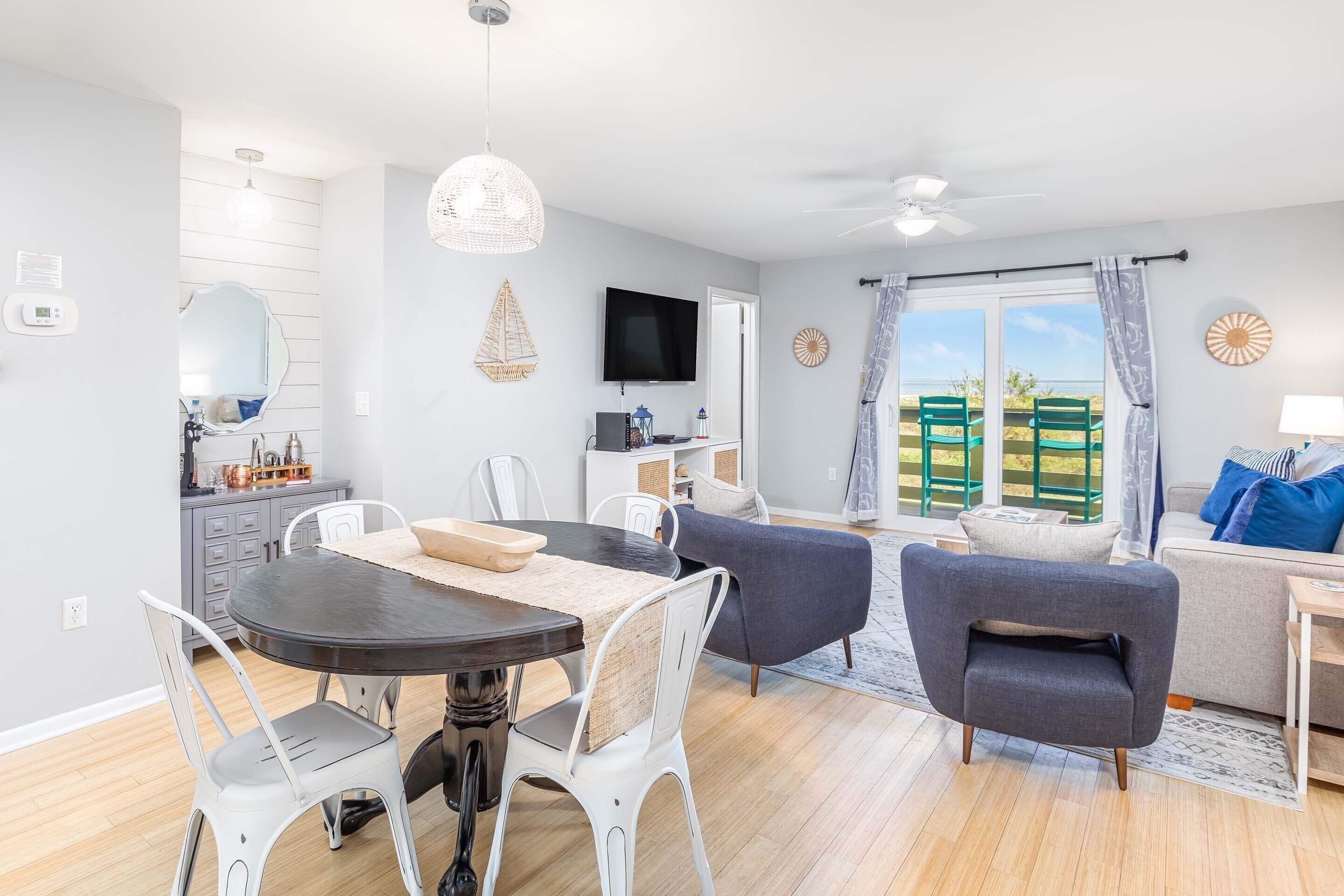 A modern living room with a dining area, a flat-screen TV, and a view of the outdoors.