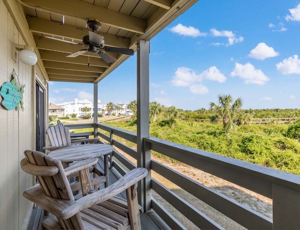 Una terraza de madera con una mesa y sillas, con vistas a un paisaje verde con palmeras y cielo despejado.