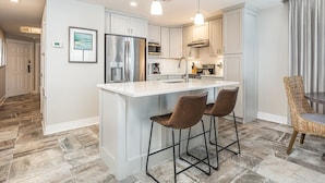 A modern kitchen with a central island, bar stools, and pendant lighting. - Ocean Song by Tybee Vacation Rentals (Tybee Island)