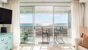 A balcony with a view of the sea, a TV, a sofa, and a dining area. - Ocean Song by Tybee Vacation Rentals (Tybee Island)