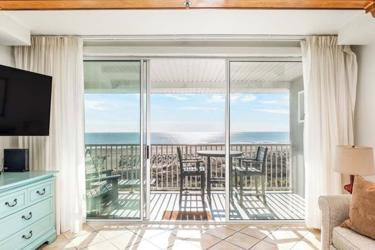 Un balcón con vista al mar, un televisor, un sofá y un comedor.