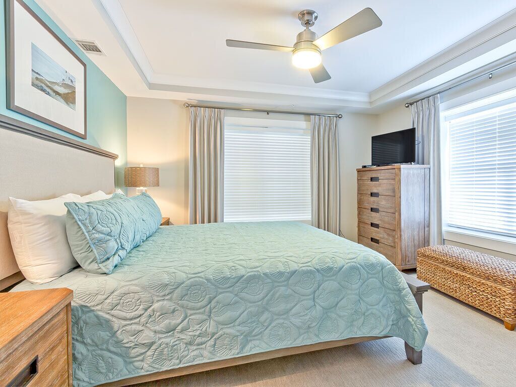 A bedroom with a bed, a ceiling fan, a dresser, a bench, and a TV.