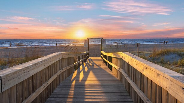 A wooden boardwalk leading to a beach with a sunset in the background. - Ocean Song by Tybee Vacation Rentals (Tybee Island)