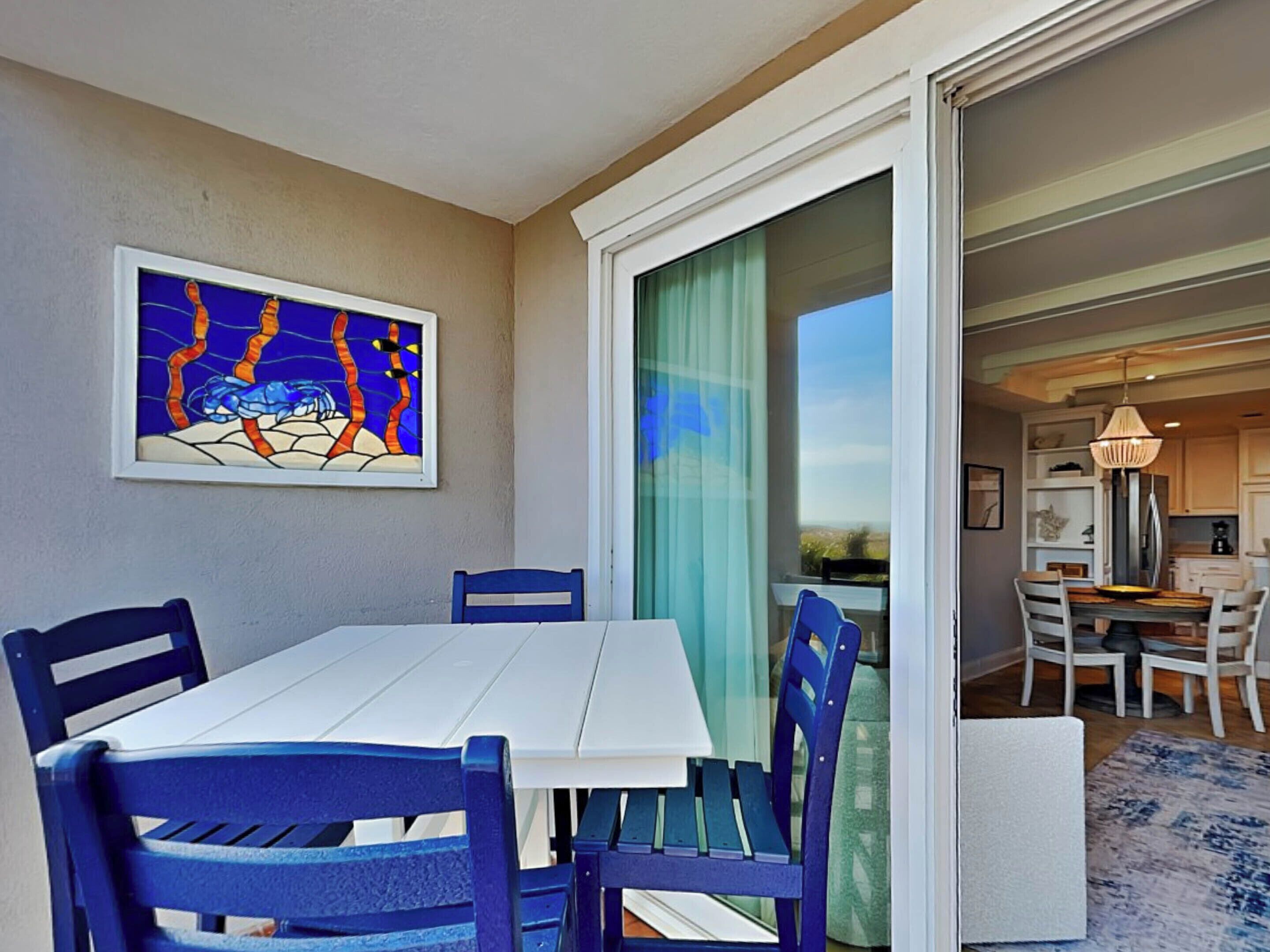 A dining area with a white table and blue chairs, a stained glass window, and a view of the outdoors.