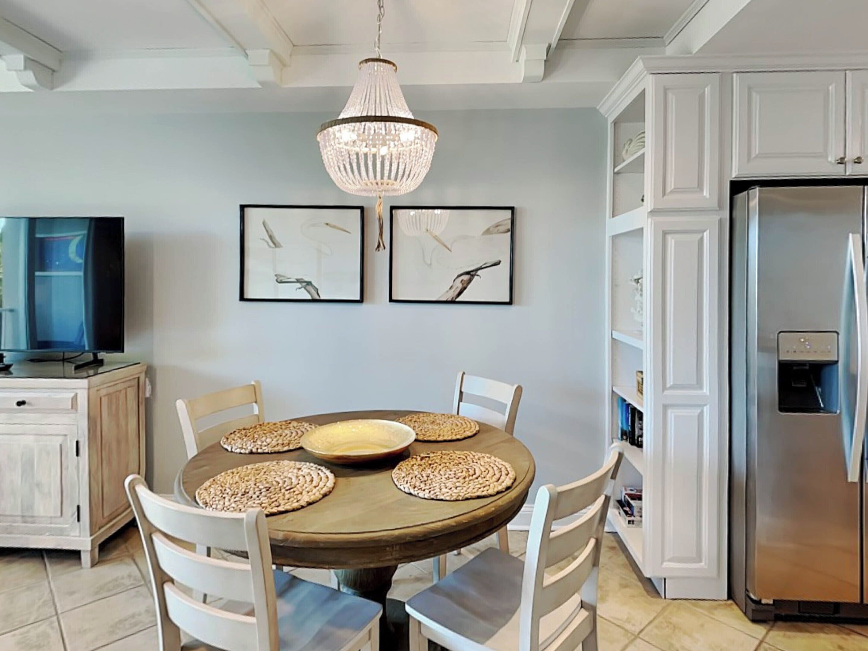 A modern kitchen with a round dining table, white chairs, a chandelier, and framed artwork on the wall.
