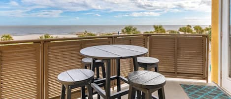 A balcony with a table and chairs overlooking the beach.