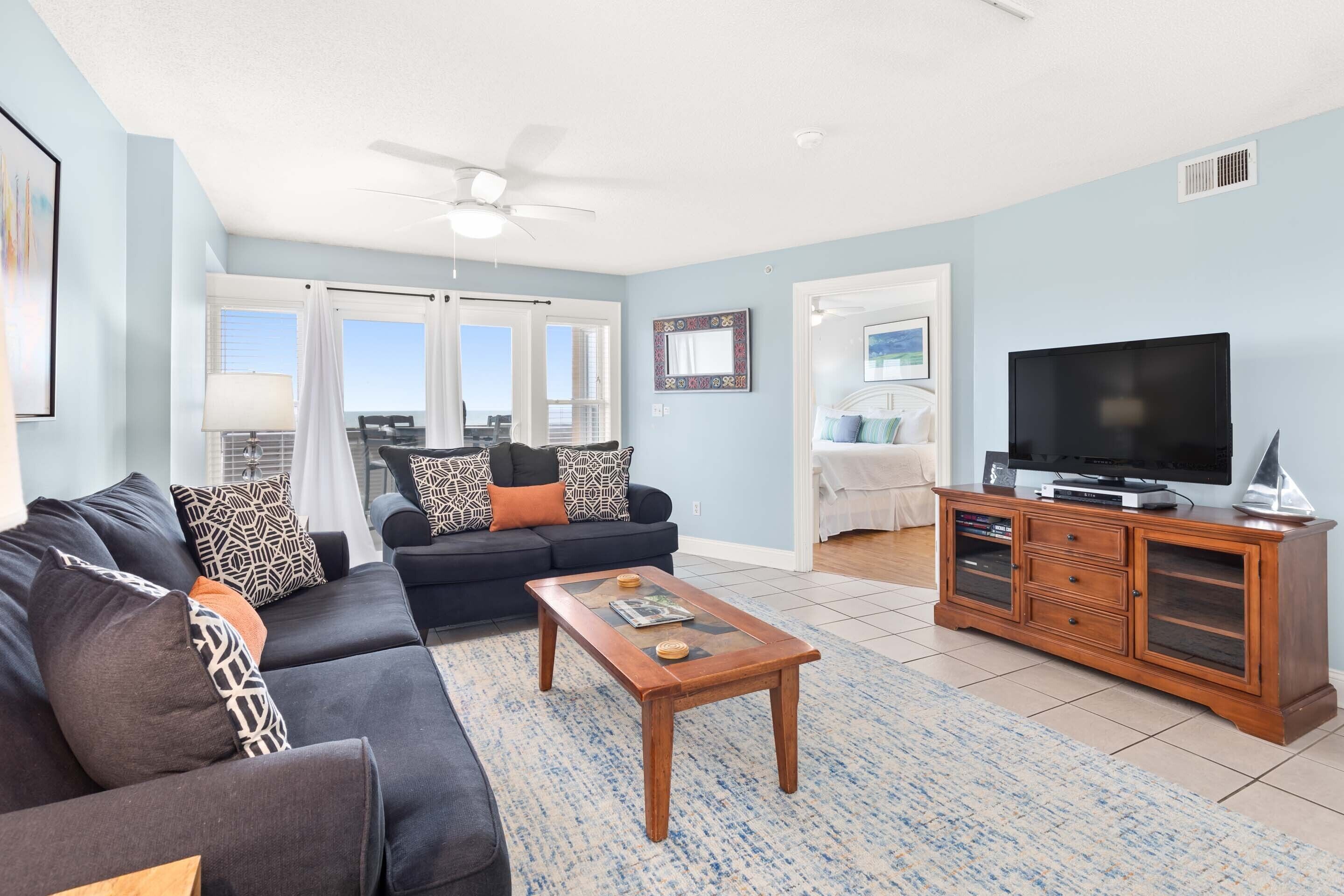 A living room with a sofa, coffee table, TV stand, and a view of the outdoors.