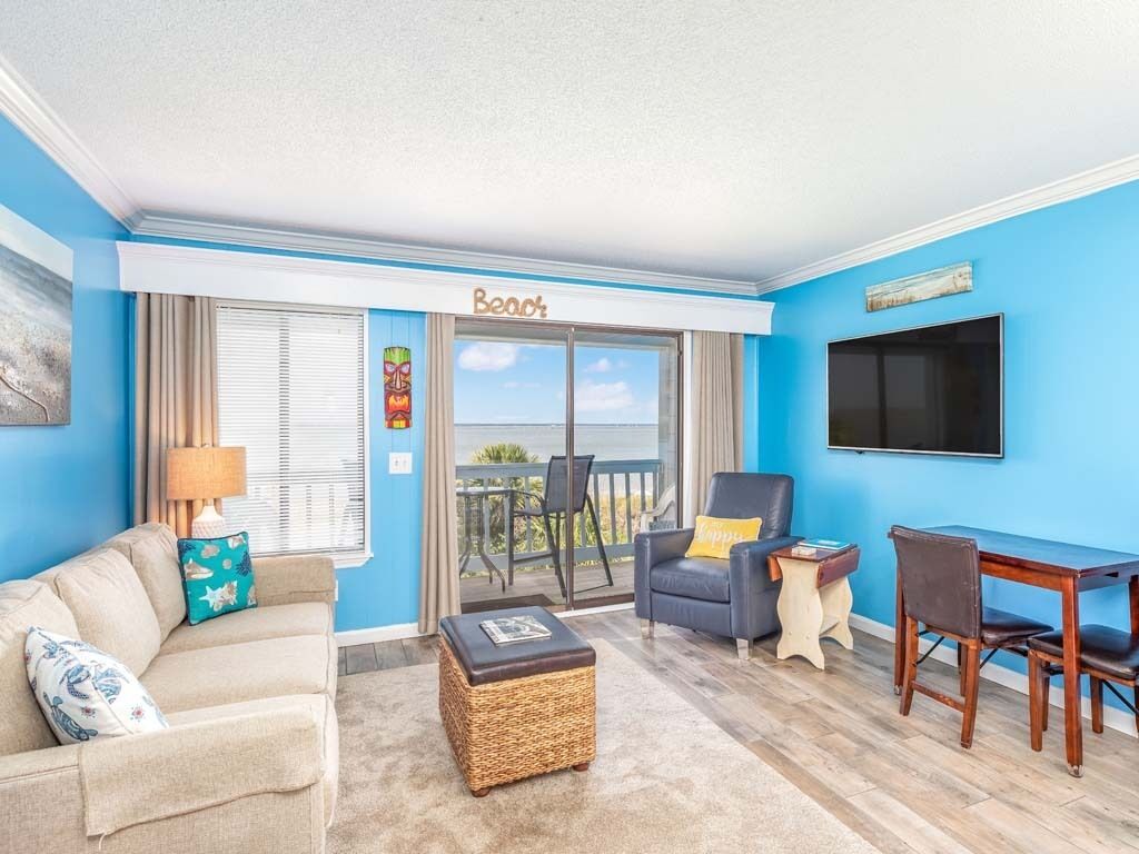 A living room with a blue wall, a sofa, a chair, a table, and a balcony with a view.