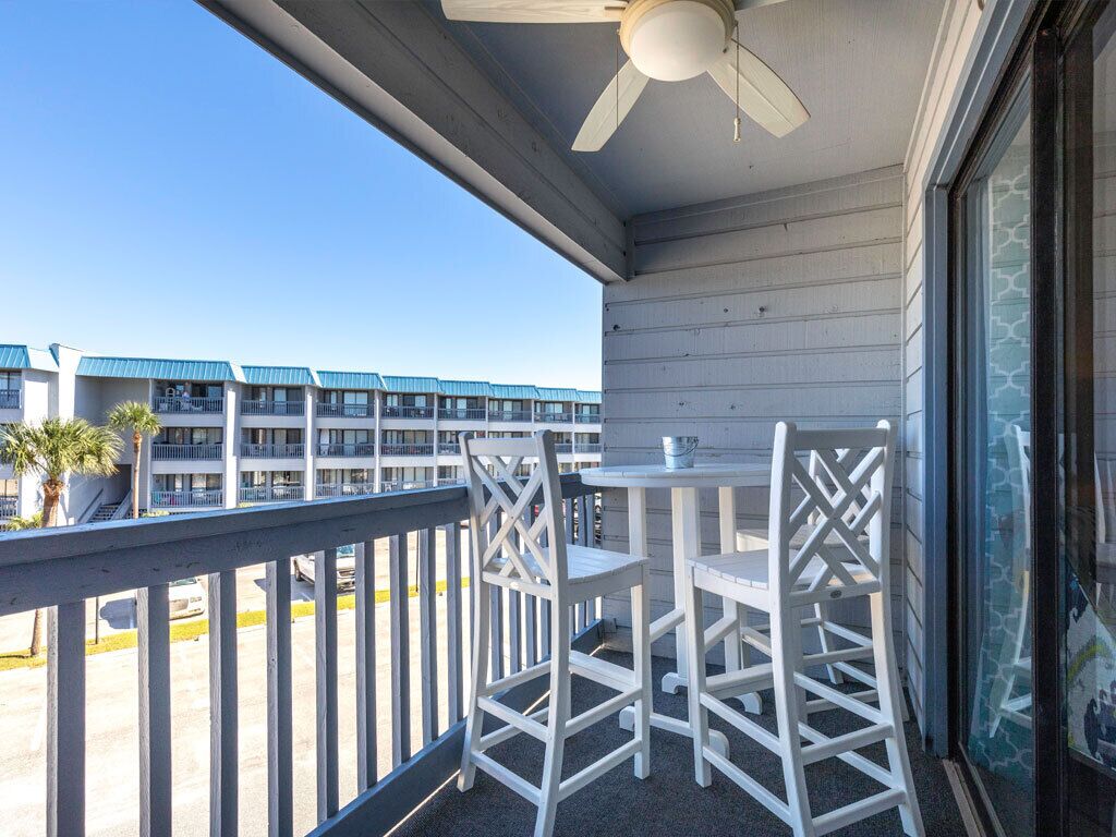 Ein Balkon mit weißen Stühlen und einem Tisch, der auf einen Parkplatz und ein Gebäude mit blauen Dächern blickt.