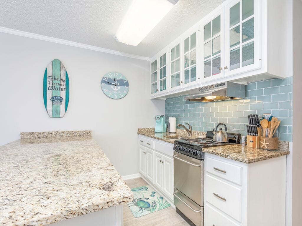 A kitchen with white cabinets, a granite countertop, a stove, and a backsplash.