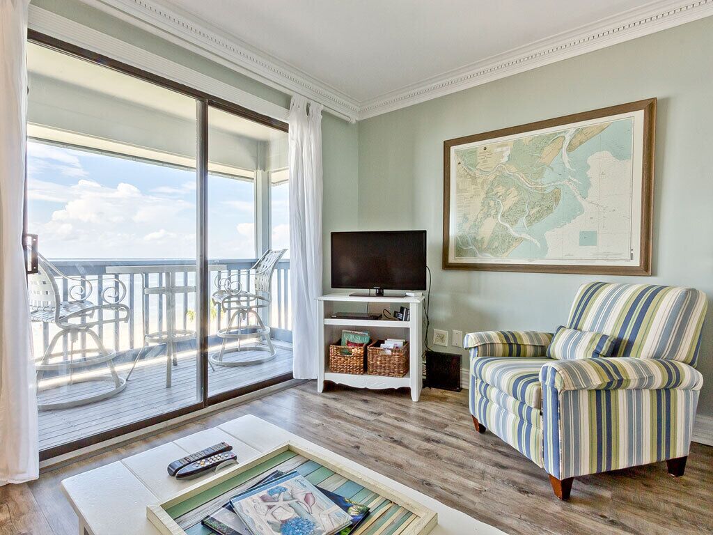 A living room with a large sliding glass door leading to a balcony, a television on a white stand, a striped armchair, and a framed map on the wall.