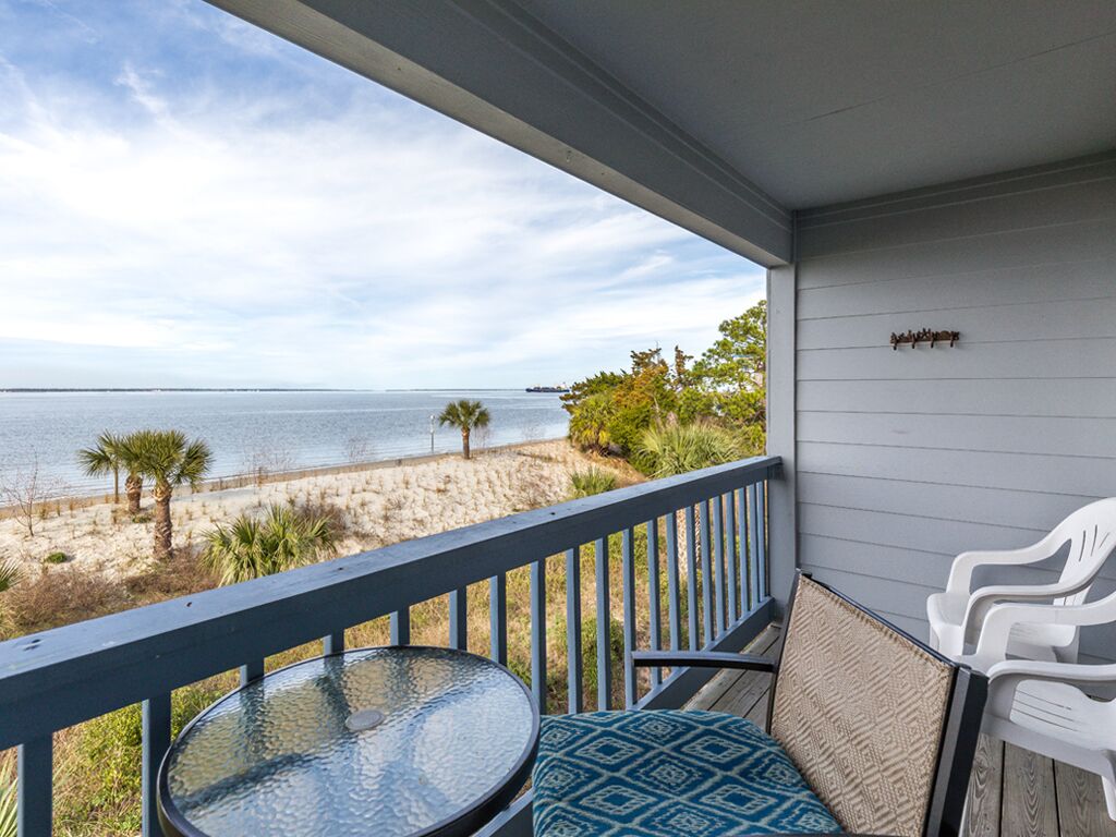 A balcony with a view of the beach and ocean, a round table, and two white chairs.