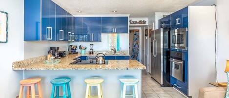 A modern kitchen with blue cabinets, a granite countertop, and a central island with stools.