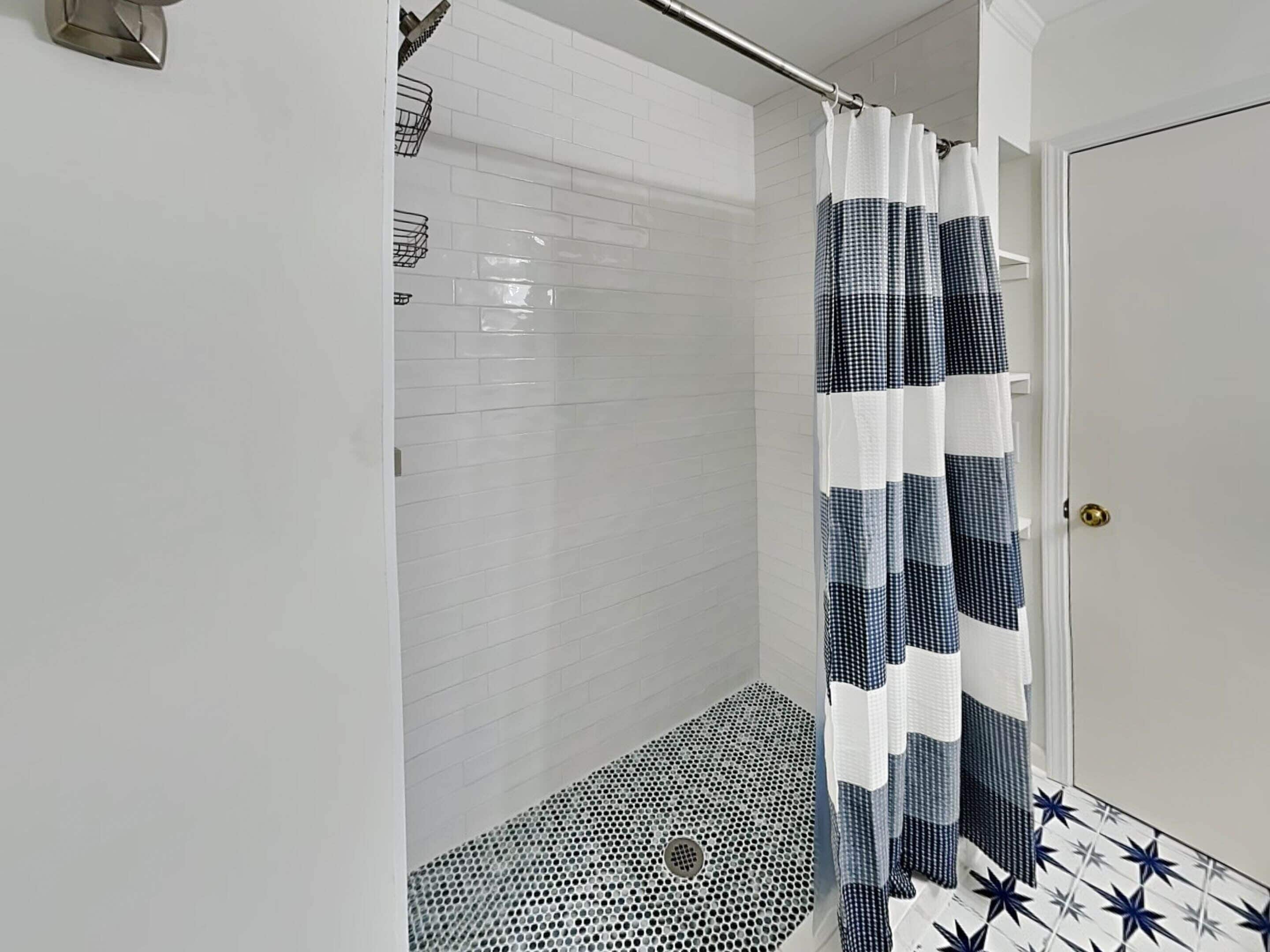 A shower with a checkered curtain, white tiled walls, and a patterned floor.