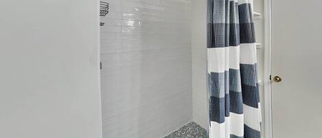 A shower with a checkered curtain, white tiled walls, and a patterned floor.