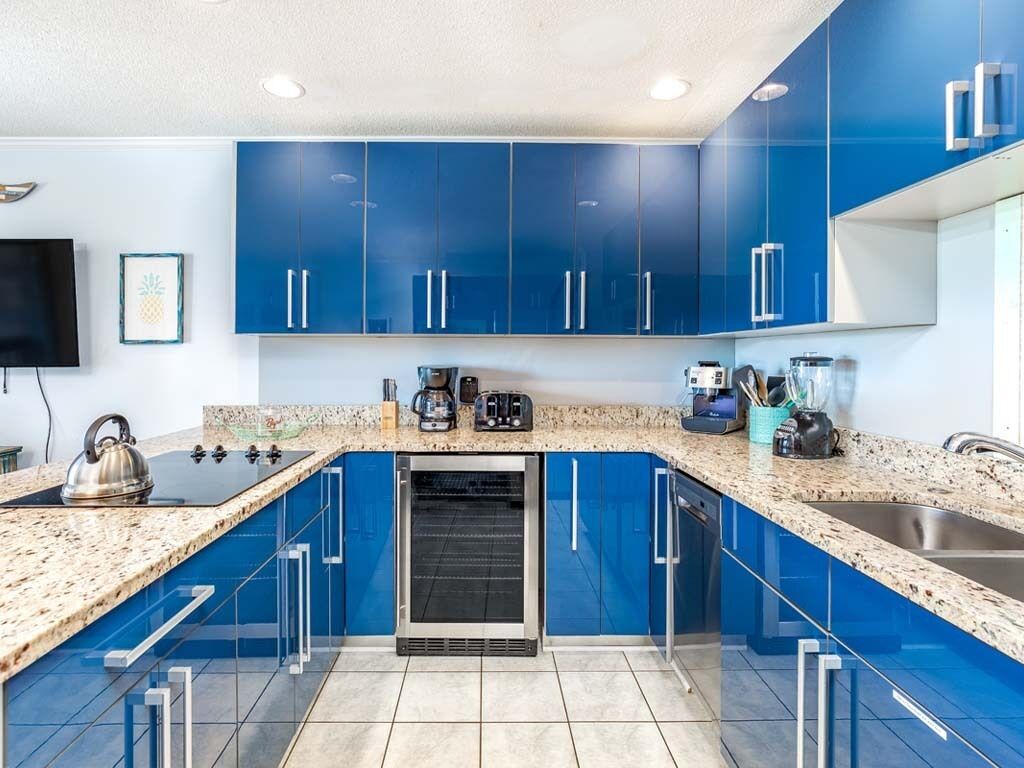 A modern kitchen with blue cabinets, a granite countertop, a built-in oven, and a stainless steel sink.