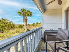 A balcony with a table and chairs, overlooking a natural landscape with a palm tree and distant horizon.