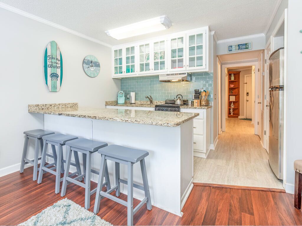 Een keuken met een centraal eiland, barkrukken, witte kasten, een klok en een decoratie van een surfboard.