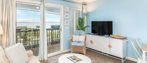 A living room with a sofa, a small table, a TV, and a balcony with a view.