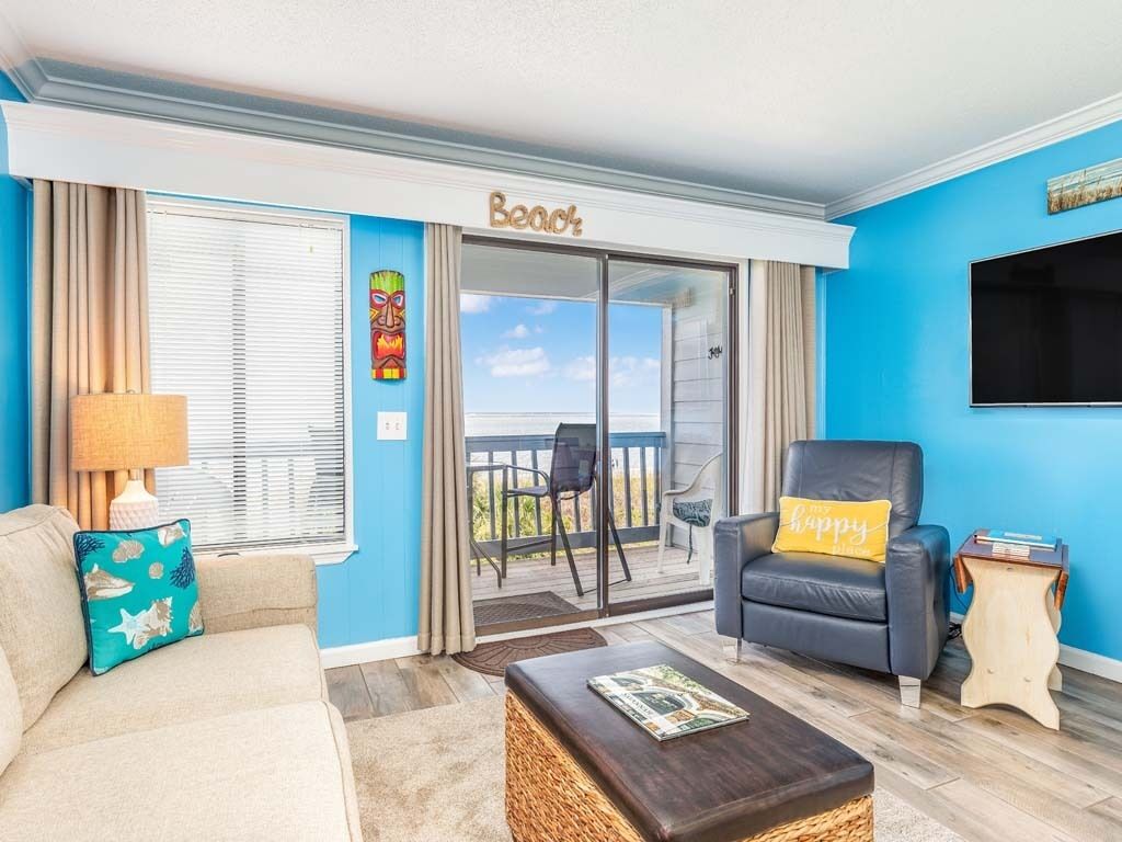 A living room with a view to the outside, a sofa, a chair, a coffee table, and a television.