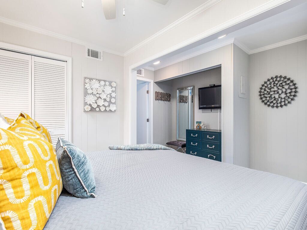 Un dormitorio con cama, cómoda, espejo y televisor montado en la pared.