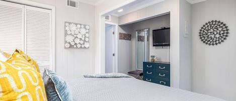 Un dormitorio con cama, cómoda, espejo y televisor montado en la pared.