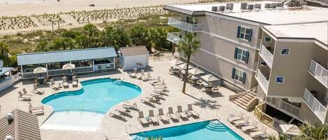 A resort with a pool area, multiple lounge chairs, and a view of the beach.