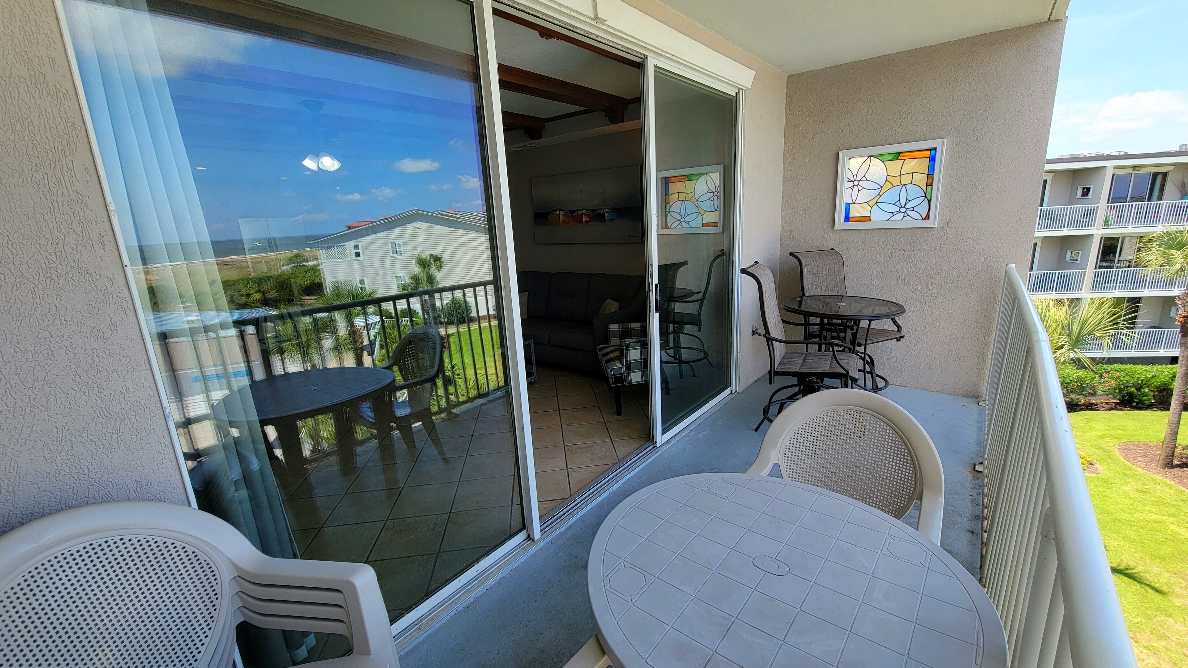 A balcony with a glass door, a small table, two chairs, and a view of a residential area.