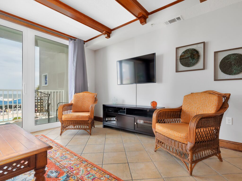 A living room with wicker furniture, a flat-screen TV, and a balcony with a view.