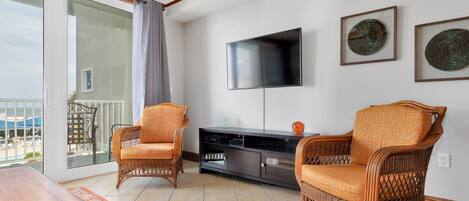 A living room with wicker furniture, a flat-screen TV, and a balcony with a view.