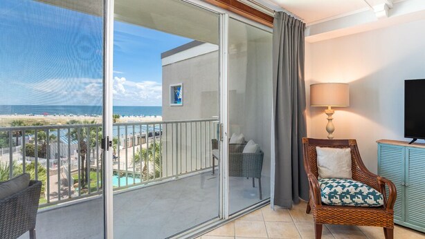 A balcony with a view of the beach, a wicker chair, a lamp, and a television. - The Vue by Tybee Vacation Rentals (Tybee Island)