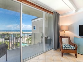 A balcony with a view of the beach, a wicker chair, a lamp, and a television.
