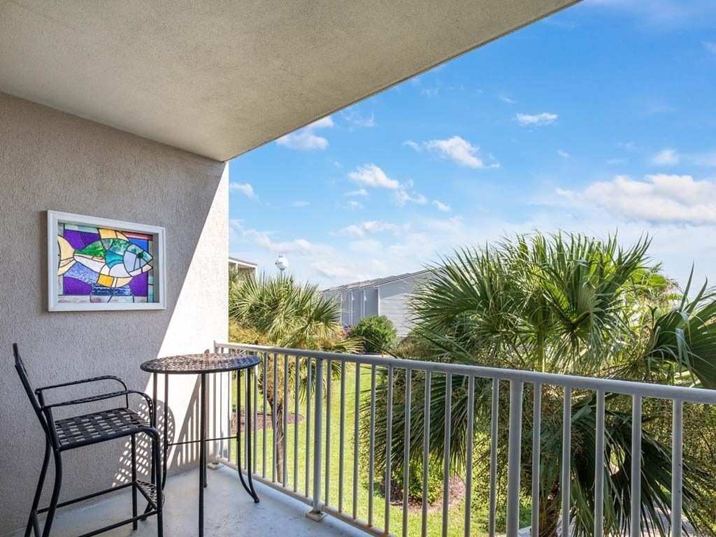 A balcony with a metal chair and table, a colorful stained glass window, and a view of a house and palm trees.