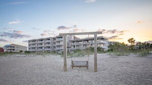 A beach with a wooden swing set and a multi-story building in the background. - The Vue by Tybee Vacation Rentals (Tybee Island)